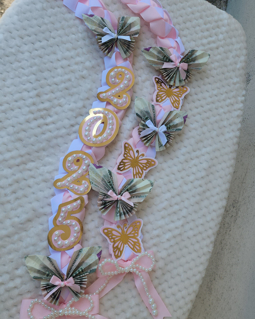 Decorative sash with pink ribbons and floral elements on a textured surface